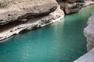 Rocky hiking trail beside turquoise pools and limestone cliffs at Wadi Shab Oman