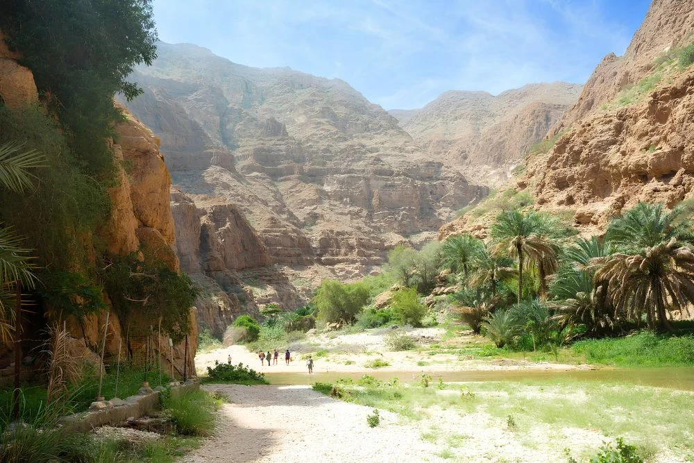 Travelers walking through the natural terrain at Wadi Shab Oman